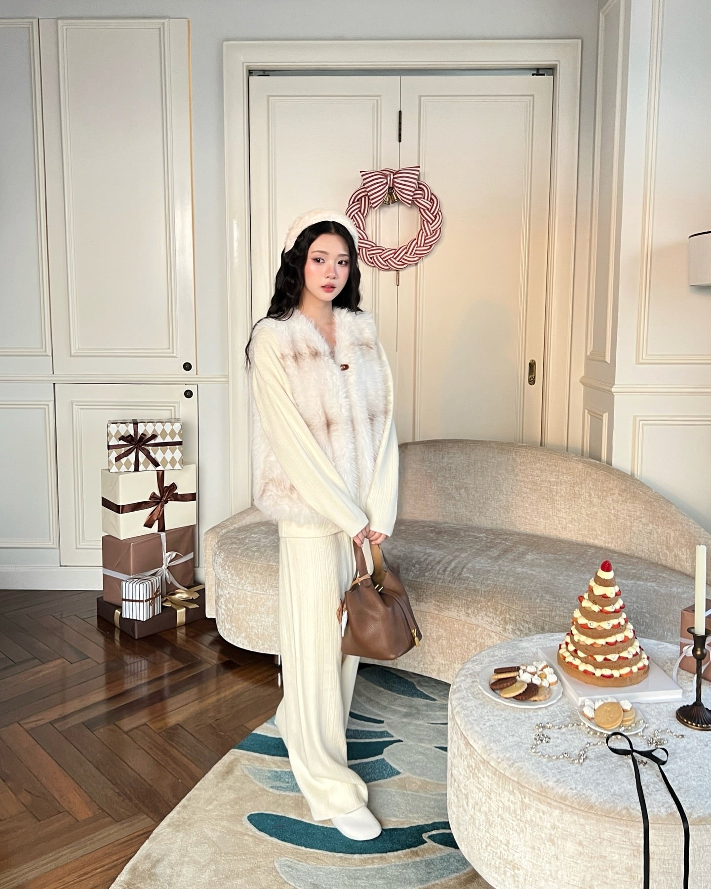The.lookbook.select的 La Neige Fur Vest ❄️ 新品優惠中，一位女士正在客廳中享受節日氣氛，客廳中有禮物、花環和節日甜點，散發著溫暖的氛圍，非常適合冬季慶祝活動。.