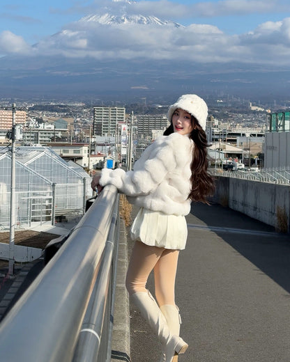 一位女士在人行天橋上為 the.lookbook.select 的棉花糖皮草大衣 (附帽子) 當模特兒，身後是城市和雪山。.