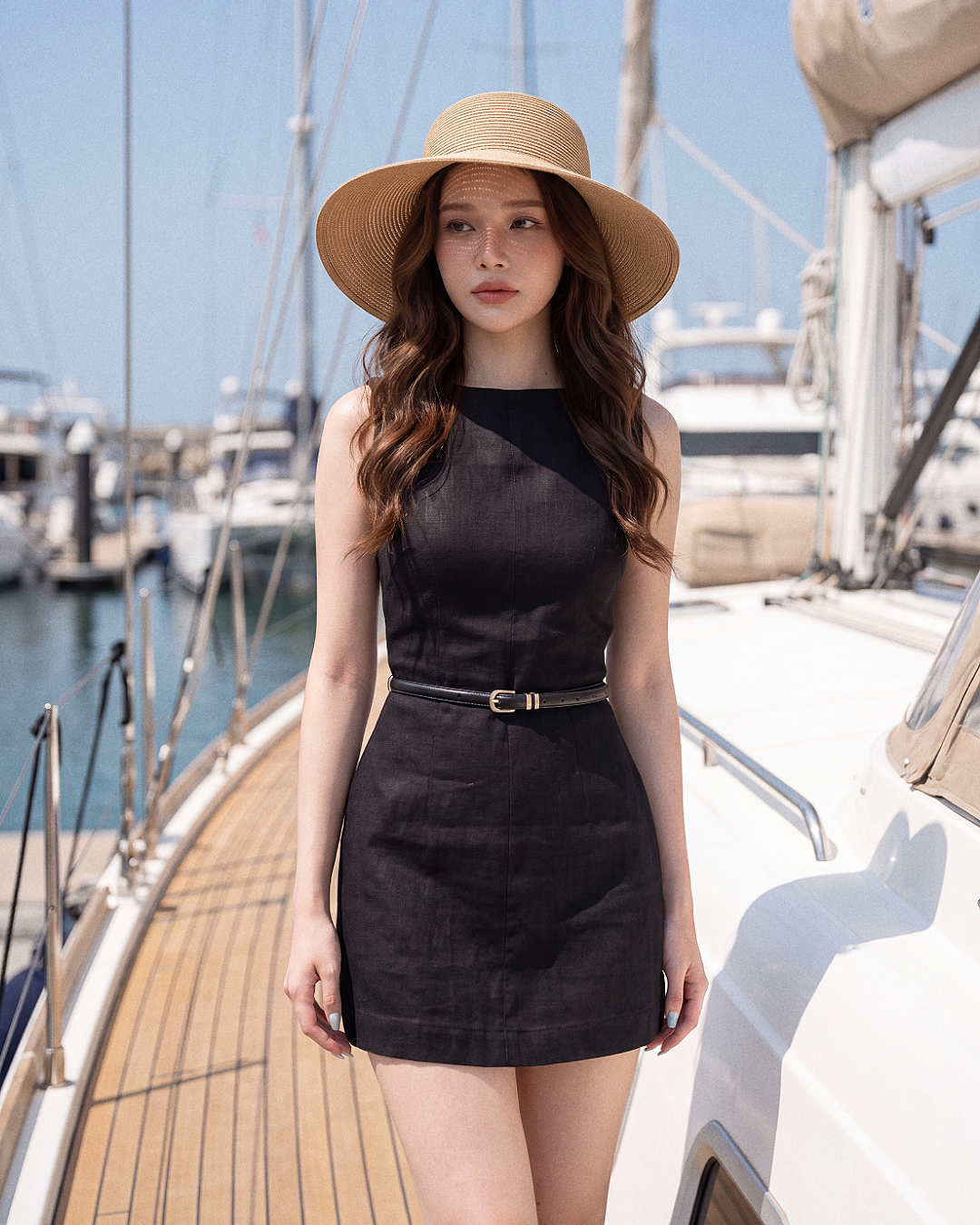 一名身穿.lookbook.select 卡普里系帶迷你洋裝、頭戴寬簷帽的女子，站在遊艇甲板上，背景中可見其他船隻與遊艇碼頭。.