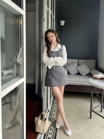 一位女士站在室內的玻璃門旁，身穿 the.lookbook.select 的 Junior Sleeveless 連身裙，手持米色手提包，背景是沙發和條紋抱枕。.