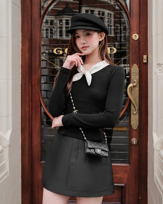 一位穿著 the.lookbook.select 的 Dear Knit Top 🖤新品優惠至 12 月 5 日、黑色短裙、貝雷帽和小挎包的女士站在一扇有玻璃面板和銅柄的木門前。.