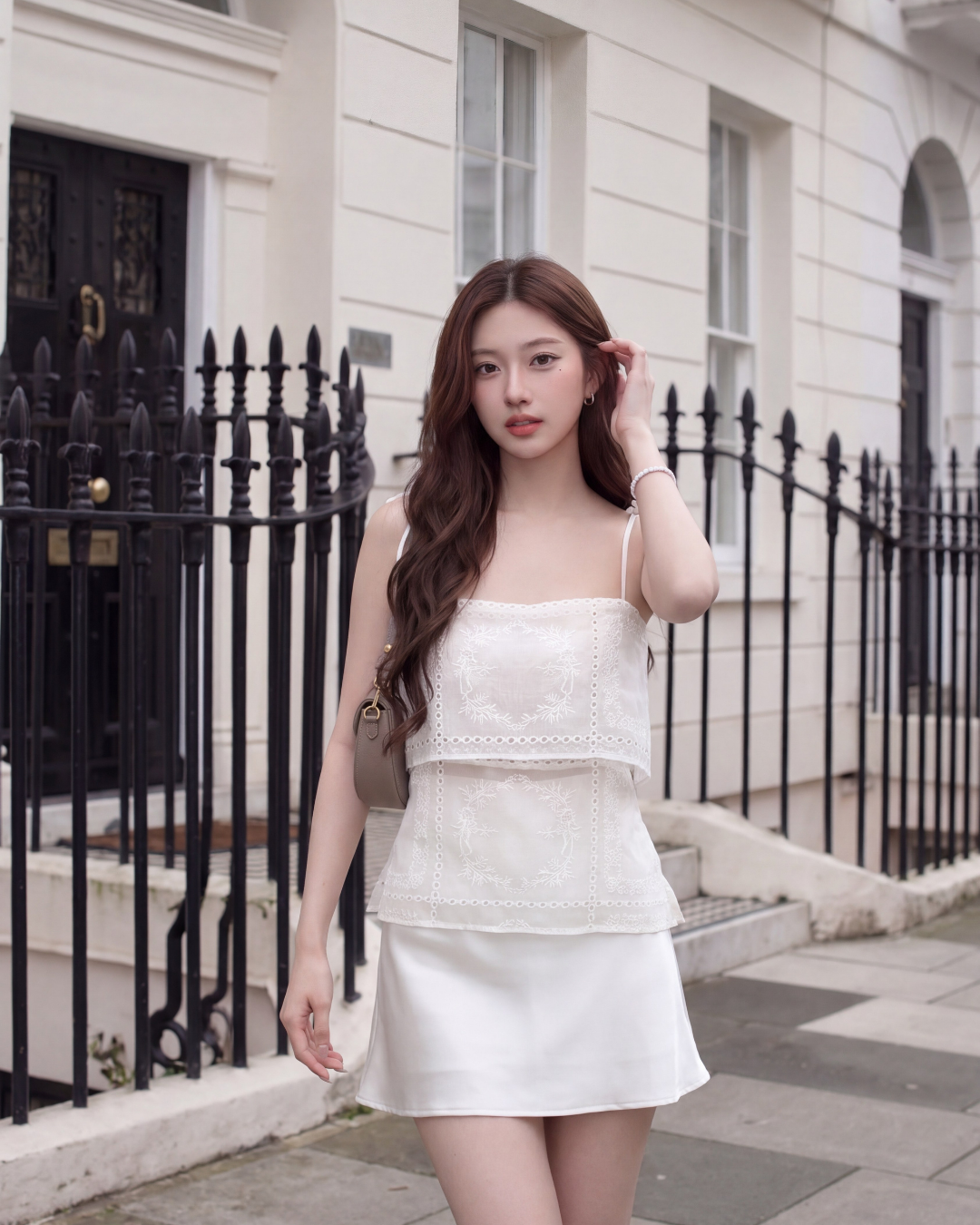 一位女士穿著.lookbook.select Heirloom Eyelet Cami 🌙新品優惠2件9折，走在一棟有黑色欄杆的白色建築前的城市人行道上。.
