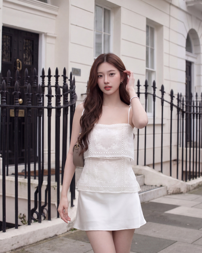 一位女士穿著.lookbook.select Heirloom Eyelet Cami 🌙新品優惠2件9折，走在一棟有黑色欄杆的白色建築前的城市人行道上。.