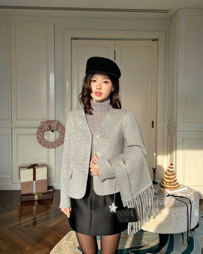 一位女士穿著.lookbook.select Snow Wool Coat❄️新品優惠和高領毛衣，搭配黑色短裙和帽子，站在室內的桌子旁，背景是蛋糕和包好的禮物。.