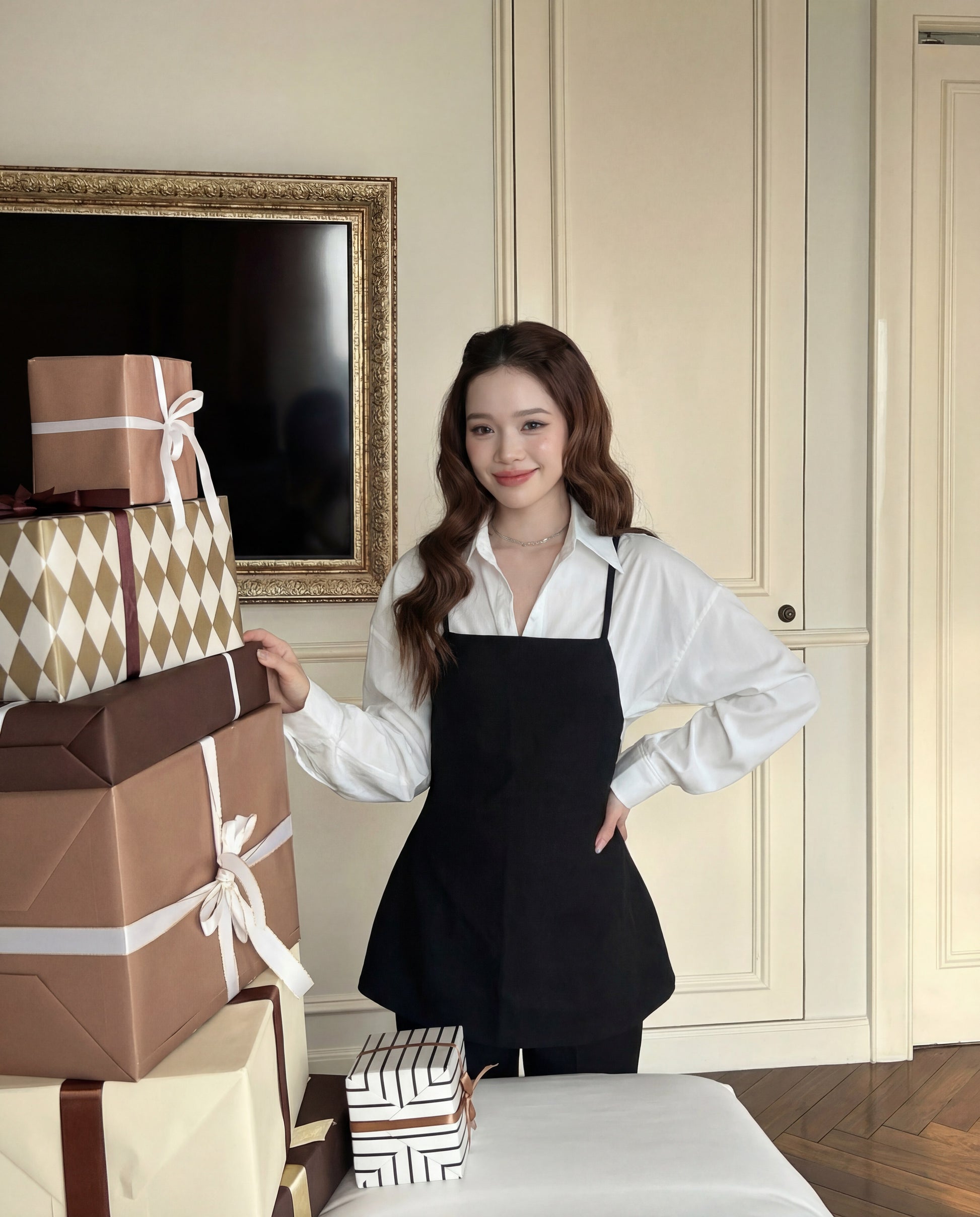 一位穿著 the.lookbook.select 設計的 Moet 褲子套裝的女士，站在室內堆滿包裝禮盒的桌子旁。.