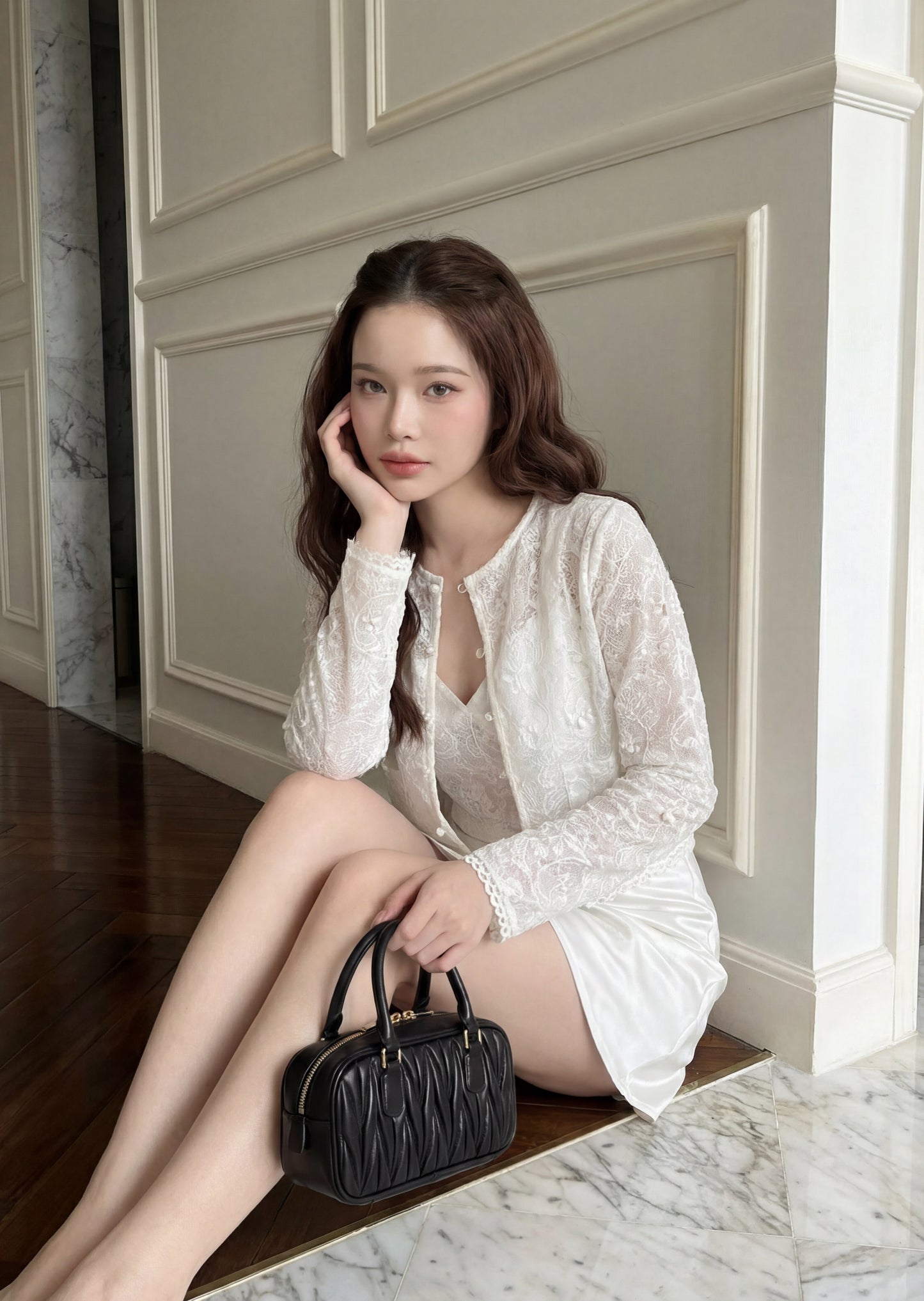 一位身穿 the.lookbook.select「Lumiere 蕾絲雙件組」（吊帶背心與外套）的女性，坐在大理石地板上，一手拿著黑色手提包，另一隻手撐在臉頰上，身後是鑲板牆。.