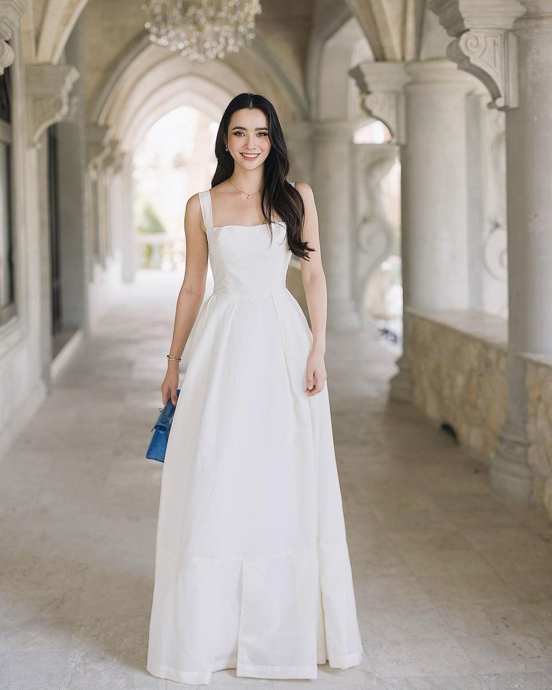 一位夢幻般的公主，穿著來自 the.lookbook.select 的白色亞麻 Leeann 長裙，站在拱門上。
